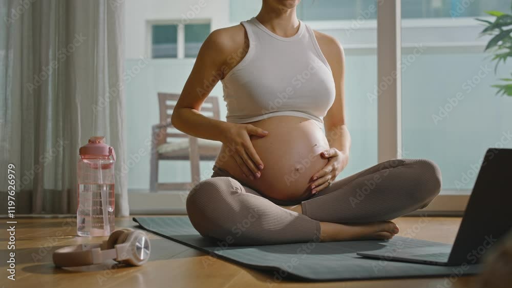 Pregnant woman practicing yoga or Pilates at home, following a lesson on her computer, relaxing and finding balance as she embraces self-care and mindfulness during pregnancy