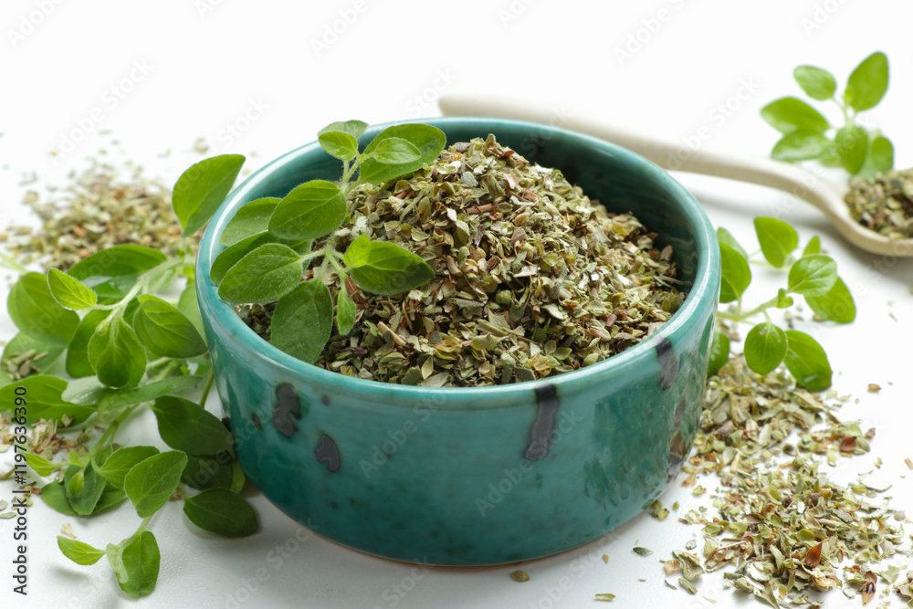 Dried oregano in bowl and green leaves on white table, closeup Dried oregano in bowl and green leaves on white table, closeup