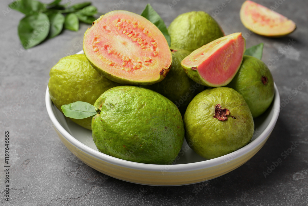 Fresh whole and cut guava fruits in bowl on grey textured table, closeup Fresh whole and cut guava fruits in bowl on grey textured table, closeup