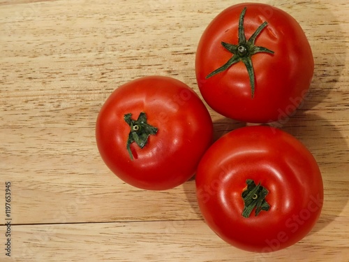 Freshly picked tomatoes resting on a wooden table, showcasing vibrant red hues and lush green stems for a rustic touch