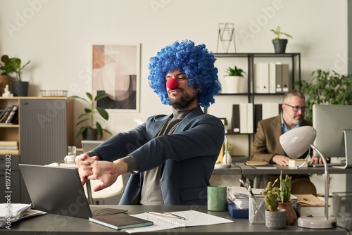 Young confident clown male analyst looking at laptop screen and stretching arms in front of himself during network photo