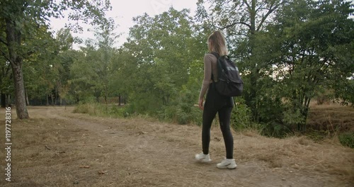 A young woman with a backpack takes a relaxing stroll through a peaceful park, enjoying the tranquility of nature.