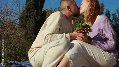 Romantic partners cuddling, embracing intimately near colorful tulips, expressing deep affection during sunny springtime garden moment.International women's day