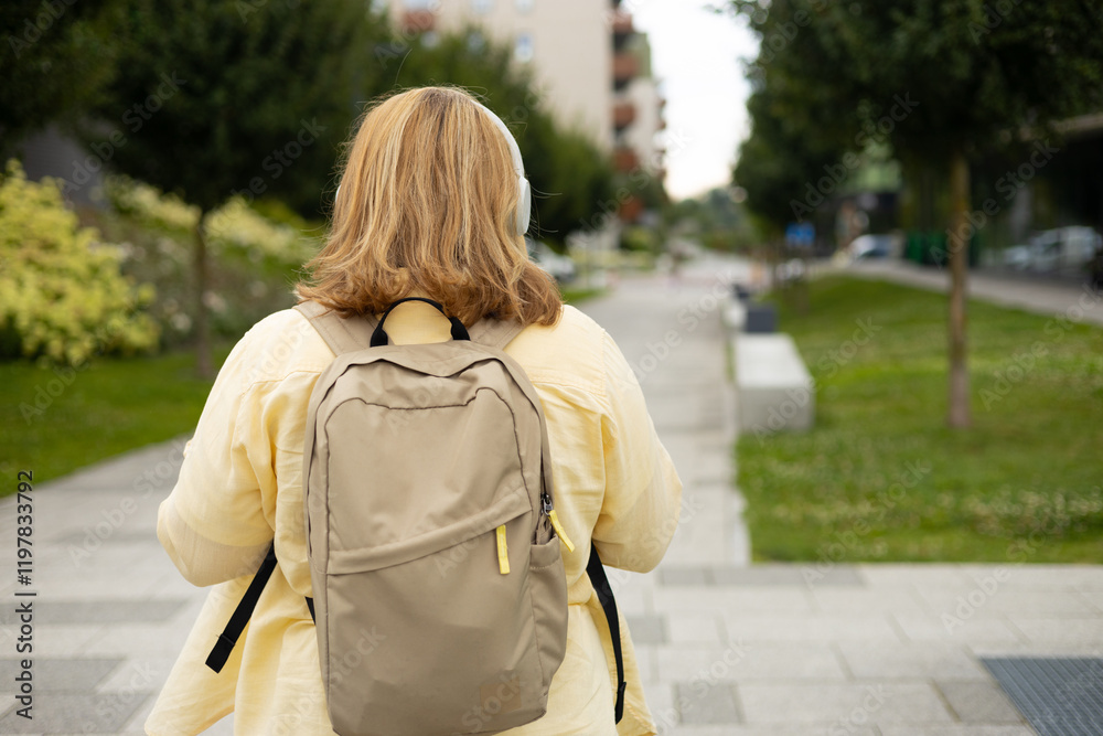 Rear view of young female tourist backpacker with headphones walking on the street. Closeup of woman resting outdoors. Urban lifestyle concept