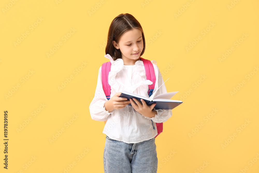 Little schoolgirl reading book on yellow background