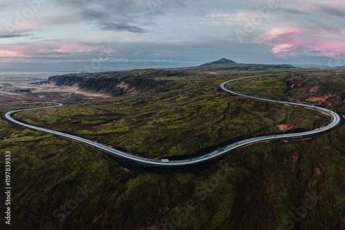 Aerial view of Iceland's Route 1 winding through Hellisheidi, surrounded by vibrant volcanic landscapes at sunrise.