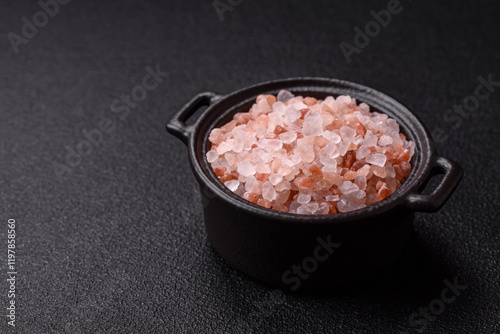 Pink himalayan salt in a black bowl on a dark concrete background