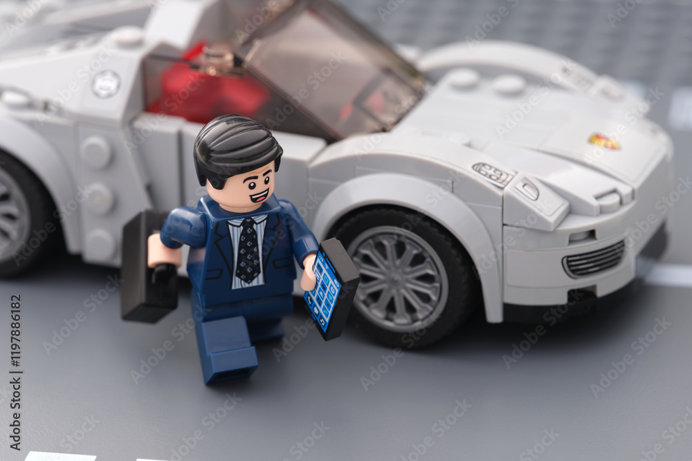 Fototapeta premium Tambov, Russian Federation - January 15, 2025 A happy Lego businessman minifigure holding a cell phone and a briefcase exiting his sports car.
