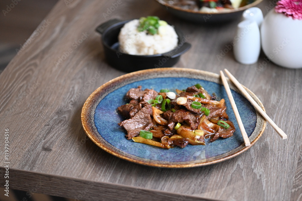 A close-up shot of a traditional Korean dish, Bulgogi, served in a rustic restaurant setting. A close-up shot of a traditional Korean dish, Bulgogi, served in a rustic restaurant setting.