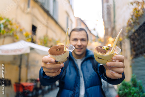 Canvas Print A man holds in her hand a traditional Italian dessert tiramisu against the background of a street in Rome in Italy