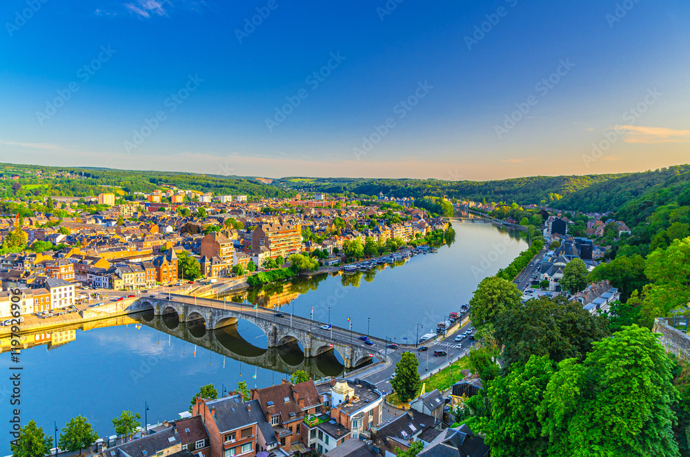 Fototapeta premium Namur cityscape with Meuse river embankment and Pont de Jambes arch stone bridge, aerial panoramic view of Namur city, skyline horizon with green forests trees on hills, Wallonia Region, Belgium