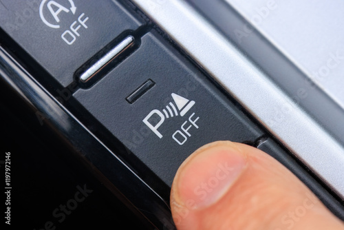 Close-up of the finger pressing parking sensor button in a modern car.
