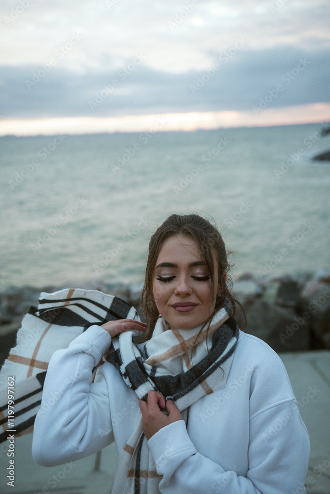 Fototapeta premium Beautiful young girl in a white tracksuit stands on the seashore in stormy weather