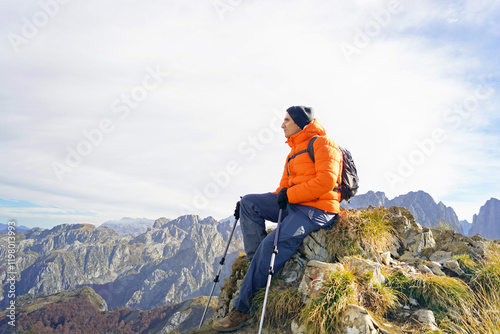 Portrait of a tourist enjoying the view on the Popadija peak in Prokletije National Park, Montenegro. Thoughtful young man sitting on a rock against the backdrop of a scenic mountain landscape