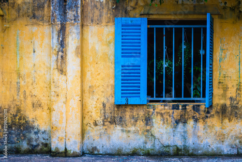 Weathered yellow wall with blue shuttered window
