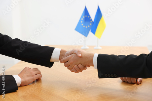 Diplomats shaking hands during meeting at wooden table indoors, closeup photo