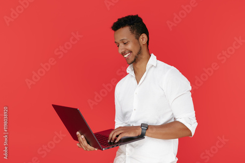 Successful african american young man holding laptop over red background.