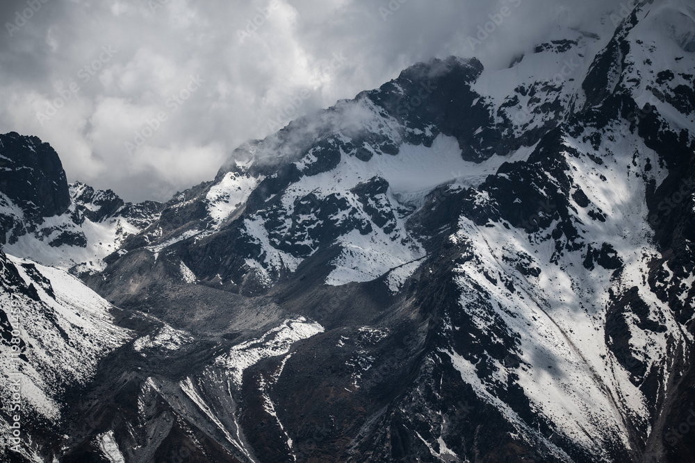Fototapeta premium Majestic snowy mountain peaks under dramatic cloudy skies in Nepal. Concept of rugged wilderness, Himalayan beauty, and alpine adventure.