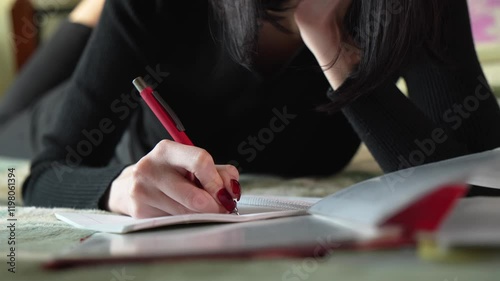 Young woman writing in notebook while lying on bed. Home environment.
