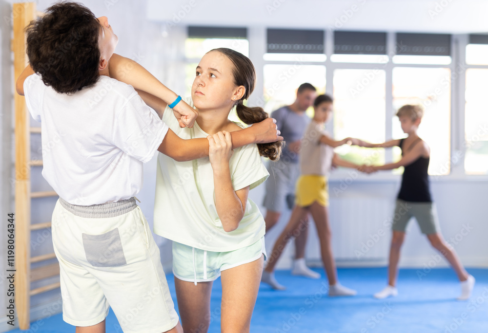 Girls and boys practicing in pair self-defence movements with female trainer supervision Girls and boys practicing in pair self-defence movements with female trainer supervision