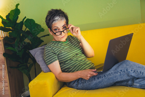Photo of nice retired female skeptical working netbook sit sofa wear green clothes enjoy cozy interior flat indoors