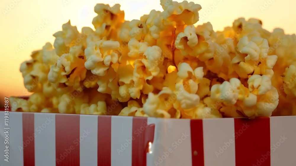 Tilt up video of a classic red and white striped popcorn box filled with fresh buttery popcorn during the golden hour, warm soft golden light