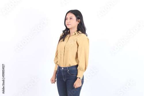 Woman in a yellow shirt and blue jeans is standing in front of a white background. She has a serious expression on her face.