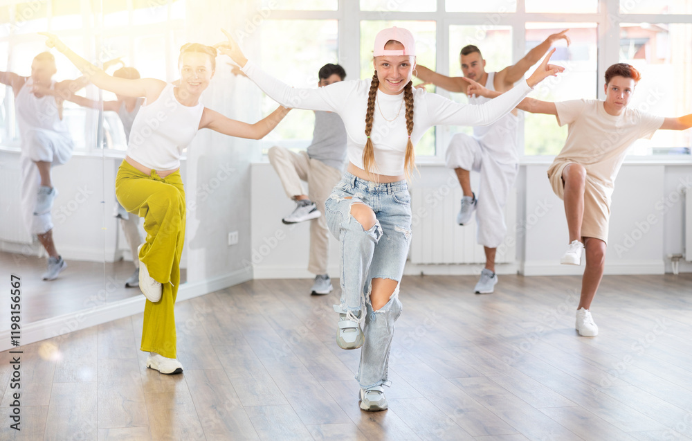 Fototapeta premium Happy teenage girl practicing hip-hop reject step in training hall during group dancing classes
