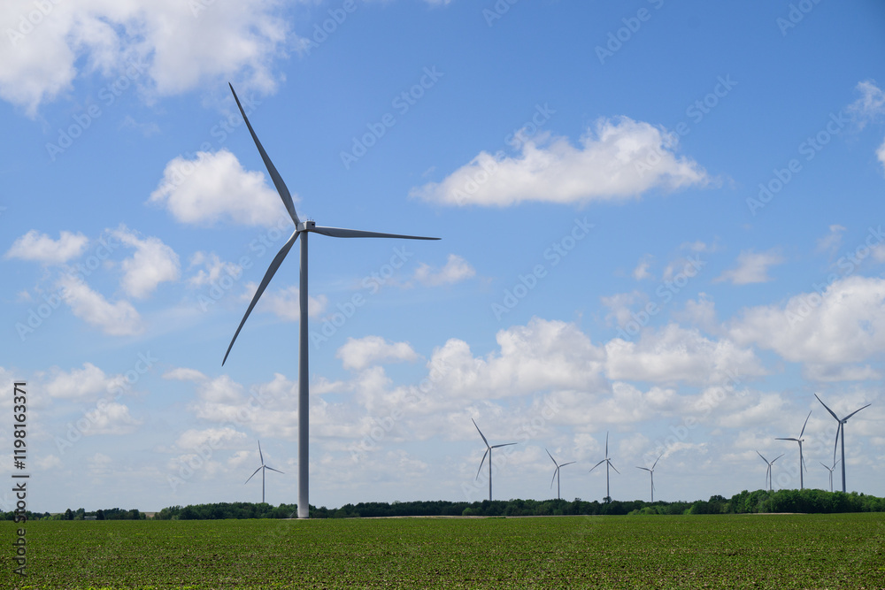 Giant white wind turbines in green field with white clouds and blue sky Giant white wind turbines in green field with white clouds and blue sky