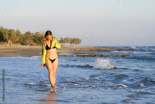 Young white woman in black bikini on the beach at sunset