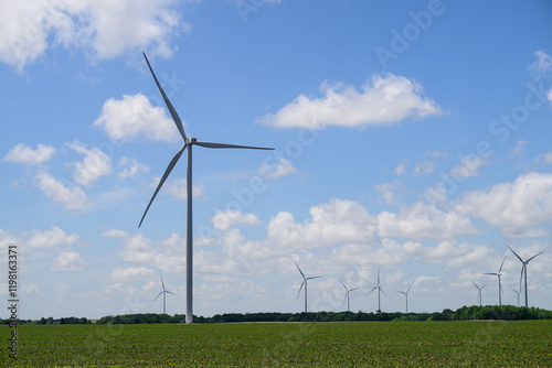 Giant white wind turbines in green field with white clouds and blue sky