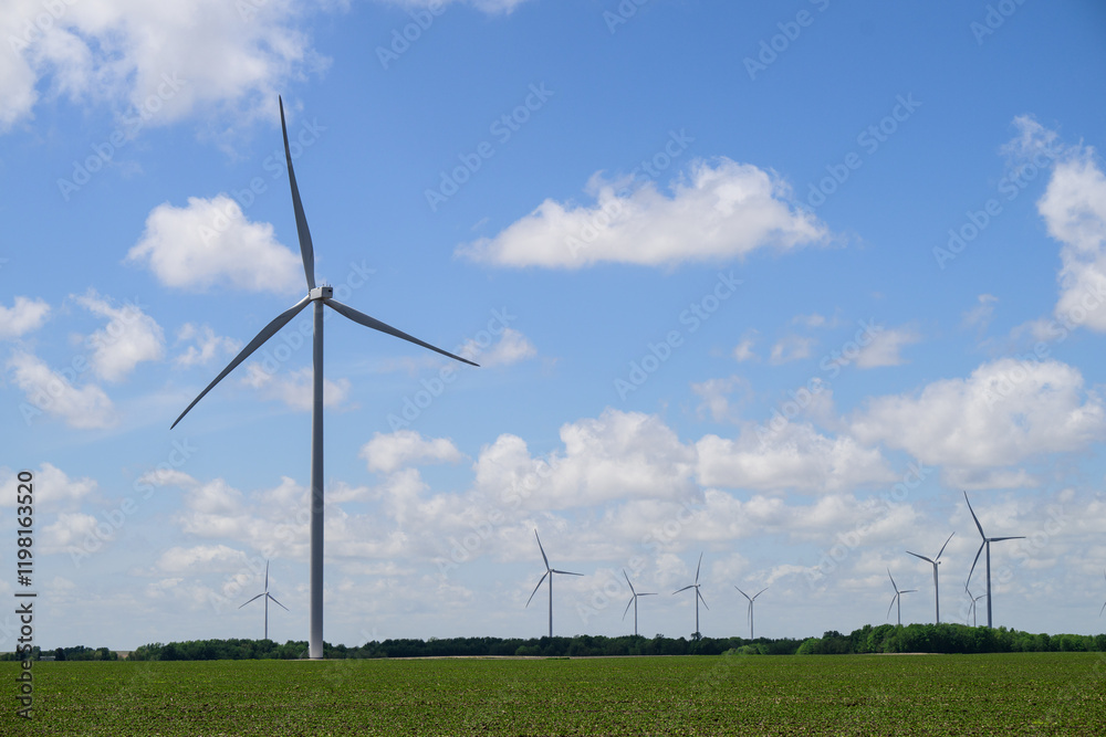 Giant white wind turbines in green field with white clouds and blue sky Giant white wind turbines in green field with white clouds and blue sky