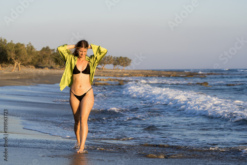 Young white woman in black bikini on the beach at sunset