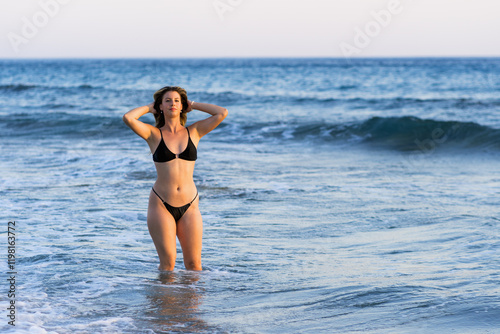 Young white woman in black bikini on the beach at sunset