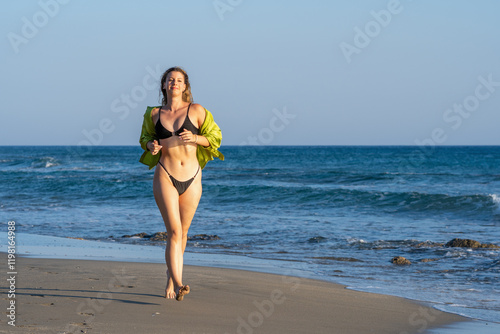 Young white woman in black bikini on the beach at sunset