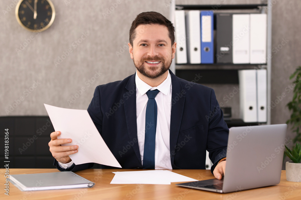 Banker holding document and working with laptop at wooden table in office Banker holding document and working with laptop at wooden table in office