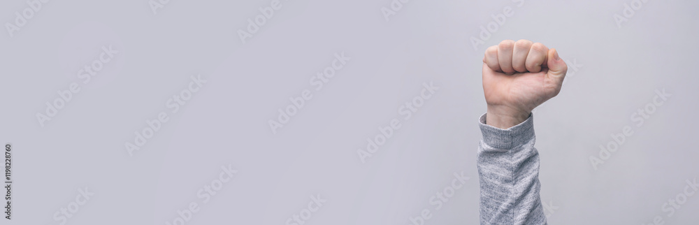 Close-up of a man in a sweater, with a clenched fist against a gray wall. The concept of struggle, protest and democracy. Close-up of a man in a sweater, with a clenched fist against a gray wall. The concept of struggle, protest and democracy.