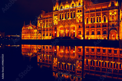 Obraz na płótnie Illuminated architectural marvel reflecting in calm waters at night. Hungarian Parliament Building showcasing symmetry, rich warm tones, and elegant historic details for use in creative projects w salonie