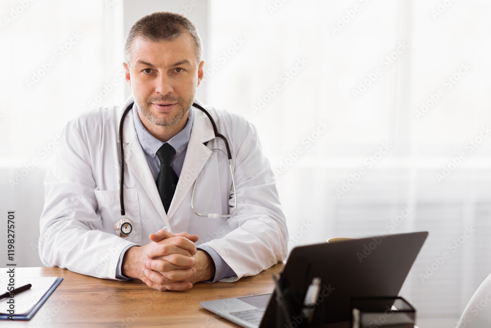 Fototapeta premium Healthcare And Medicine Concept. Portrait of mature clinician sitting at desk with laptop looking at camera