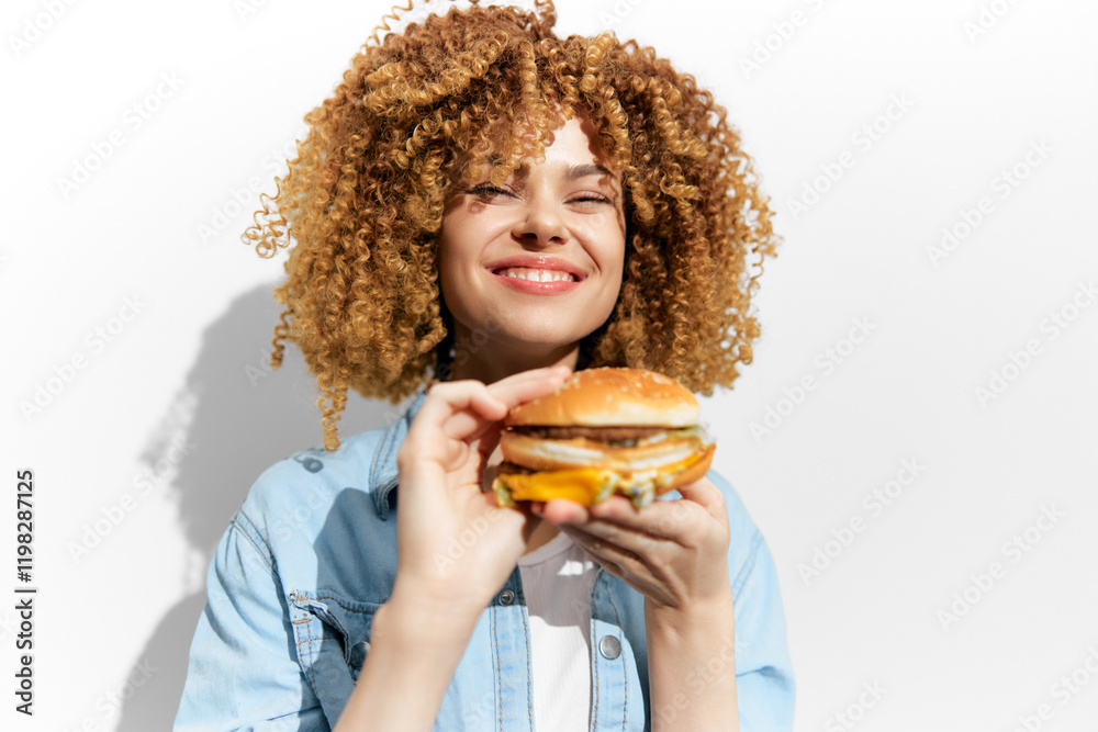 Young woman with curly hair joyfully holding a burger against a white background, representing healthy eating and happiness through food Young woman with curly hair joyfully holding a burger against a white background, representing healthy eating and happiness through food