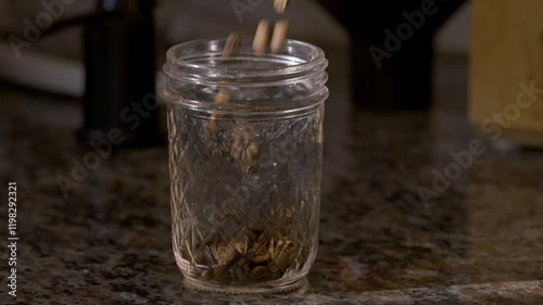 Coffee beans pouring into a glass jar in slow motion.  Close up view of light roasted whole bean coffee being stored in a glass mason jar.