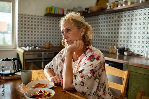 Woman deep in thought at kitchen table with breakfast photo