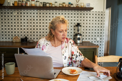 Mature woman doing financials during breakfast at home kitchen table photo