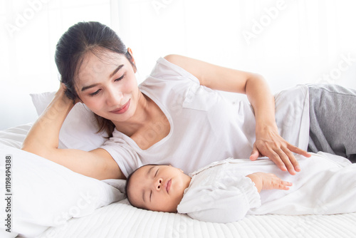 Asian young mother lullaby newborn baby on bed, single mom lying down next to adorable infant and looking with love. Women and toddlers 0-1 month sleeping, nurturing moment in soft natural lighting. photo