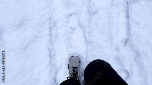 Women's feet are walking in black pants and gray boots, walking through a snowdrift leaving footprints. Viewing angle from above. High quality 4k footage