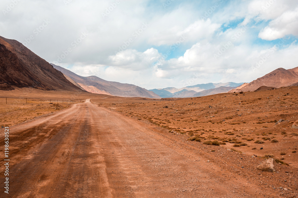 Naklejka premium A dirt road in the desert with a cloudy sky in the background