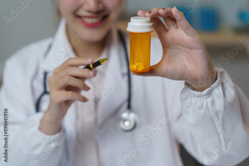 Smiling female doctor showing a pill bottle while holding a pen, likely explaining prescription details or medication instructions in a hospital setting