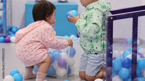 Two Young Children Playing with Colorful Plastic Balls in Indoor Playground, Siblings Sorting Toys Together
