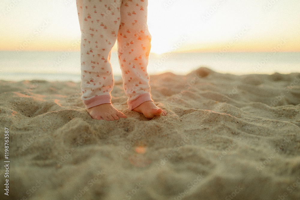 Fototapeta premium Child's feet in the sand on the beach at sunrise