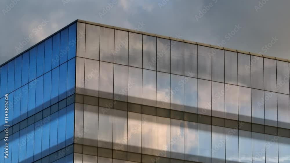 High-quality closeup of the top corner of a modern corporate office building with glass windows reflecting a blue sky and clouds. Features a slow descent down several floors, showcasing sleek design.